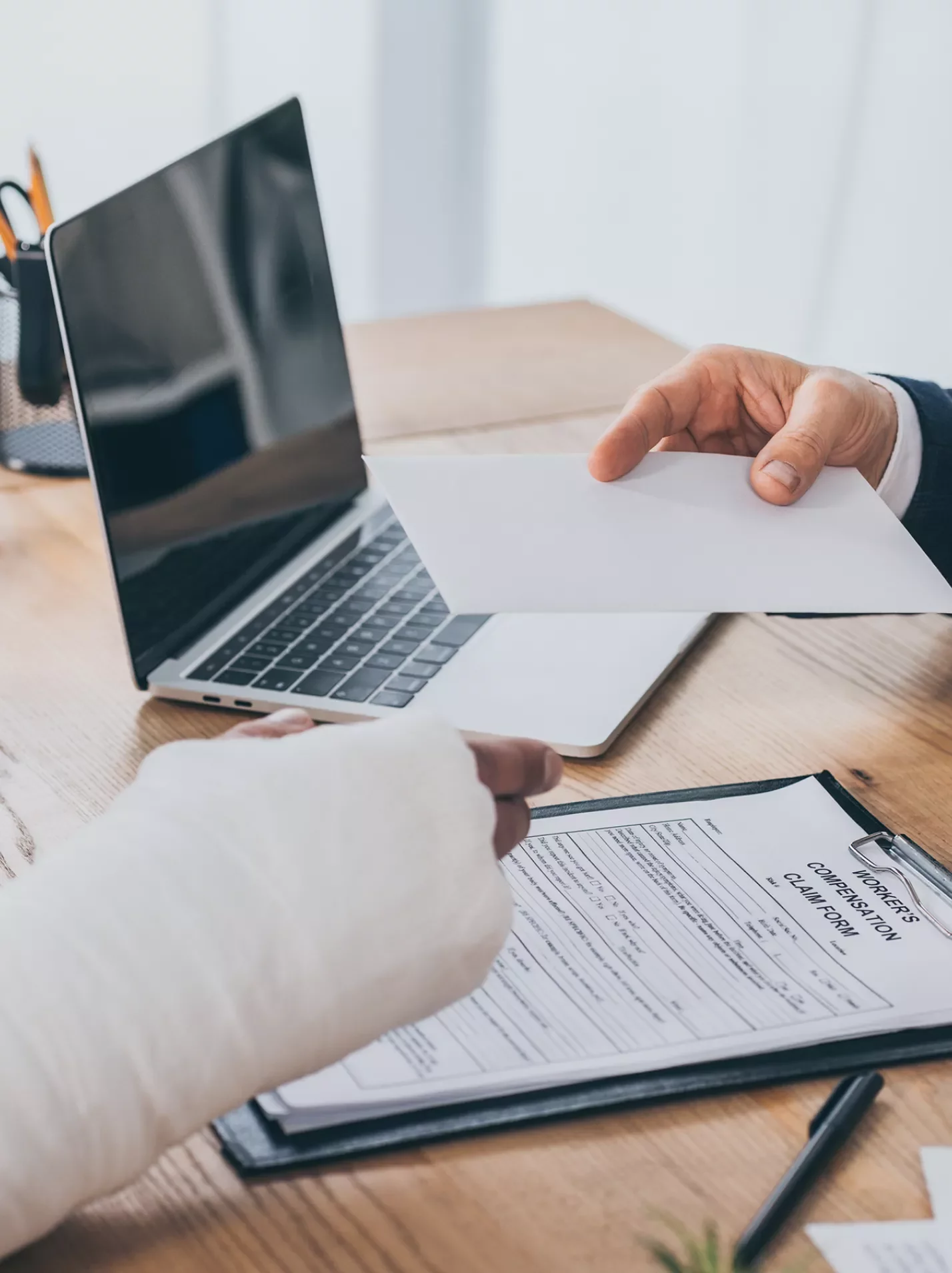 Arm in a cast taking paperwork from a person wearing a suit across a desk