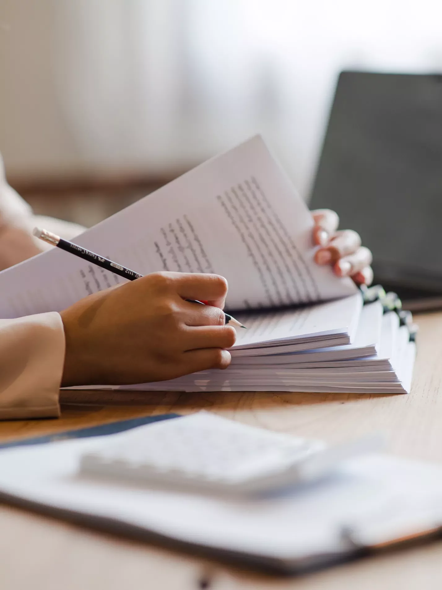 Hands on a desk looking through paperwork with a clipboard and laptop