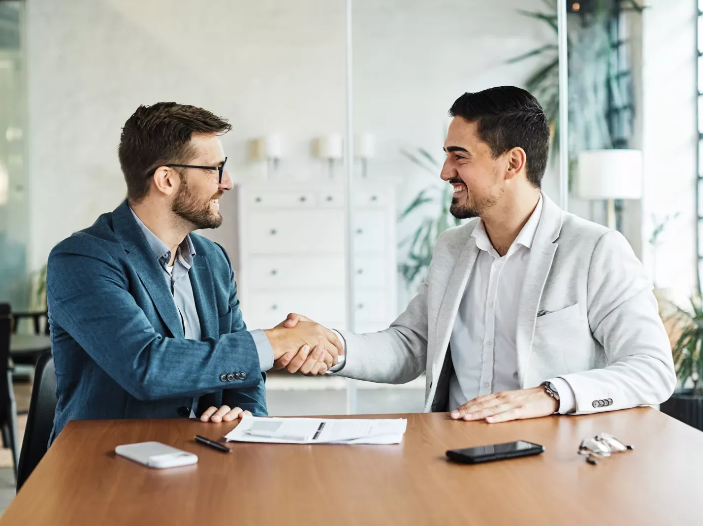 Two men at a table shaking hands over paperwork