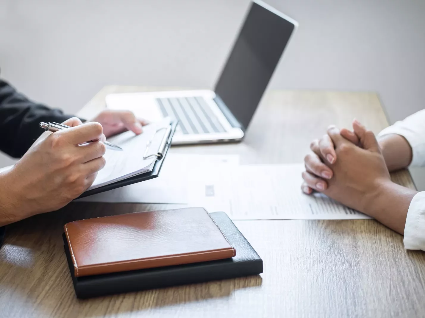 Hands of people facing each other across a desk with a laptop and files