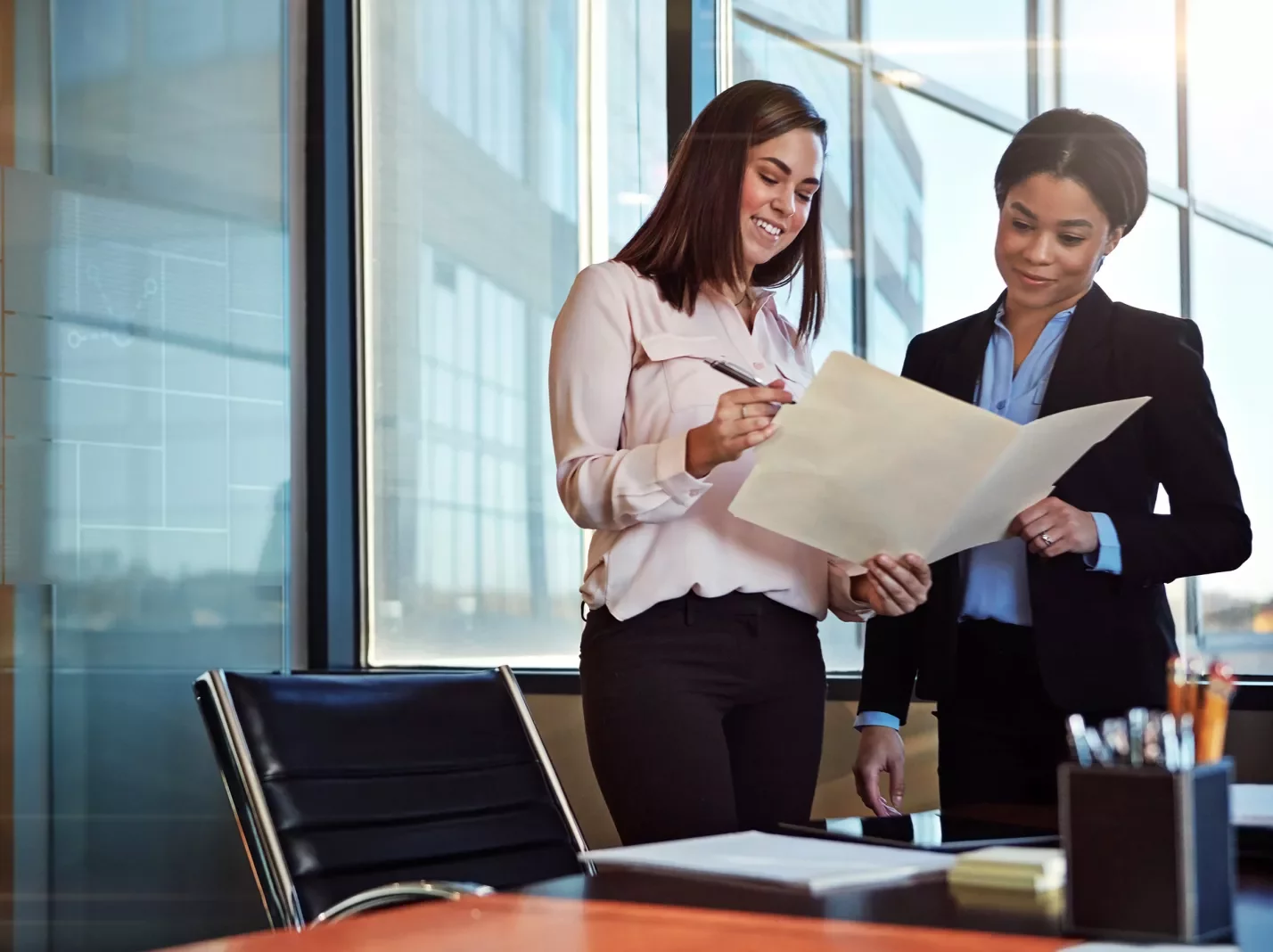 Two women standing next to a desk reviewing a folder of paperwork