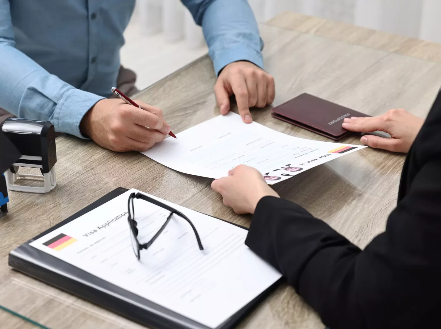 Visa paperwork on a desk being passed from one person to another with a passport