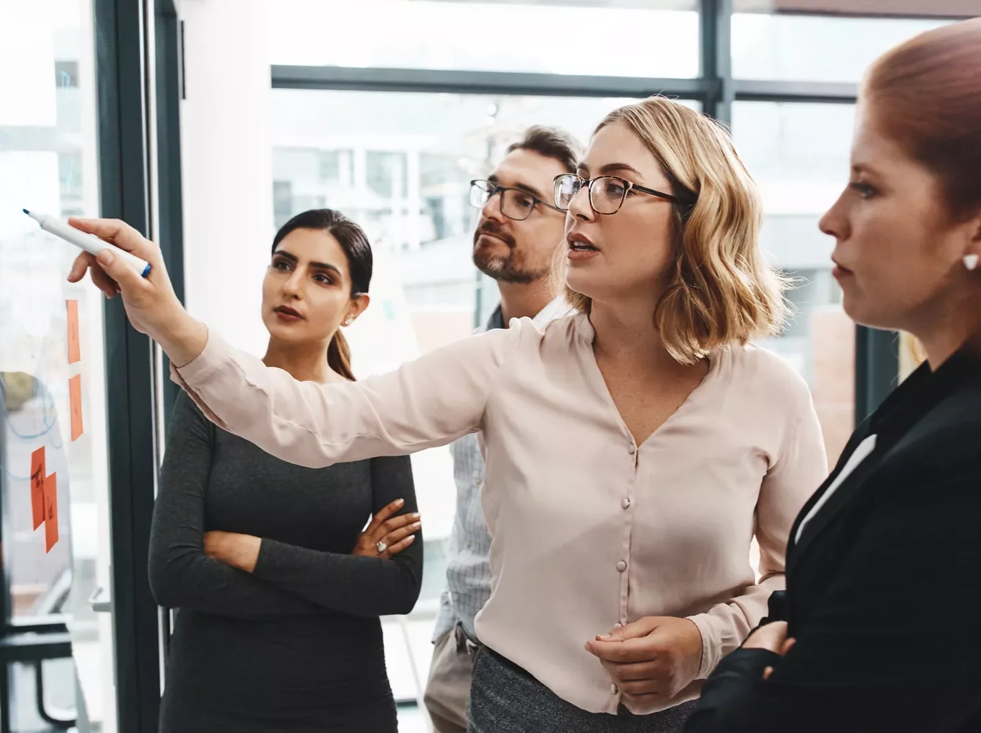 Woman pointing at a whiteboard management meeting with three other people