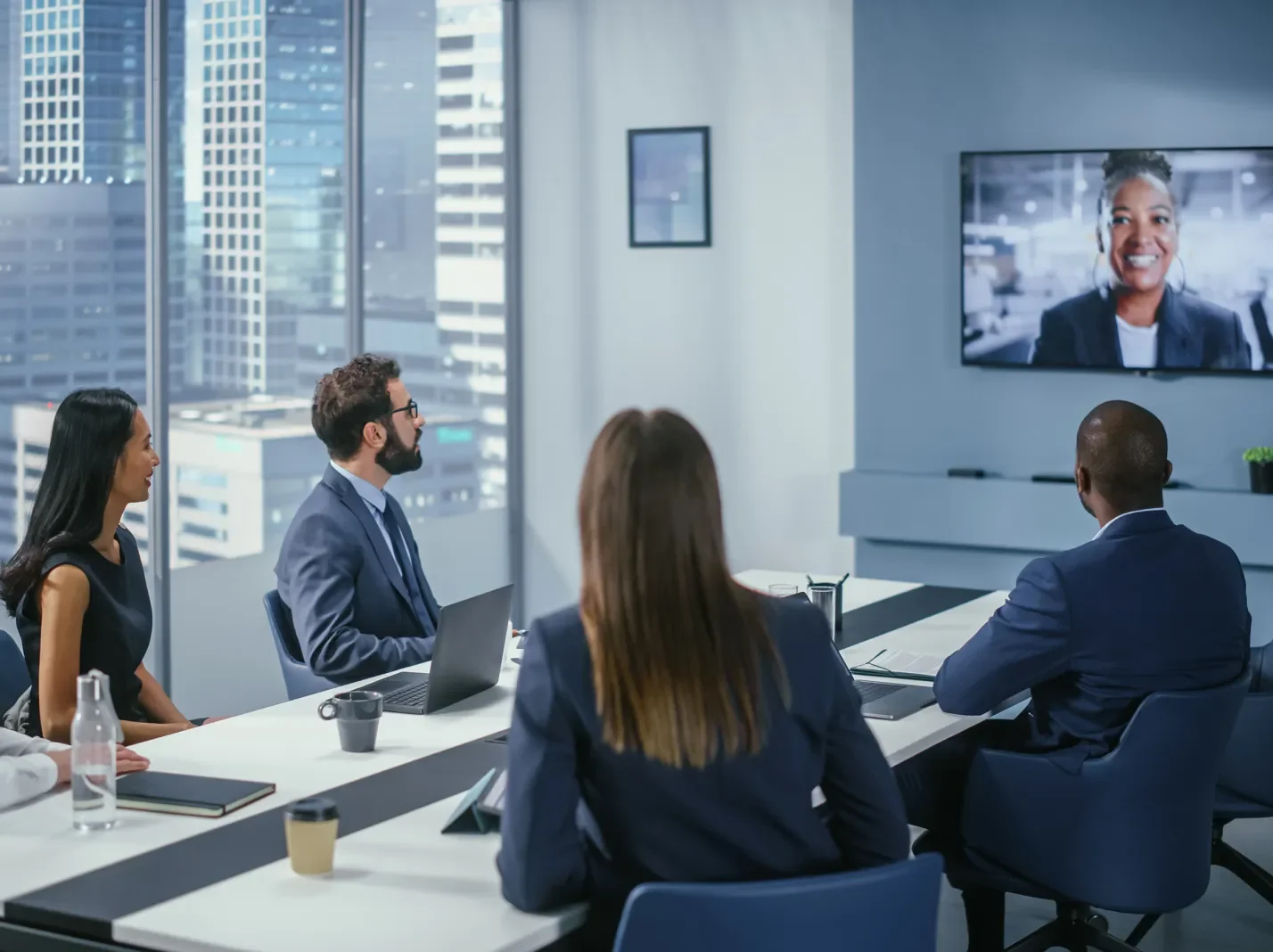 People around a conference room table looking at another participant on screen