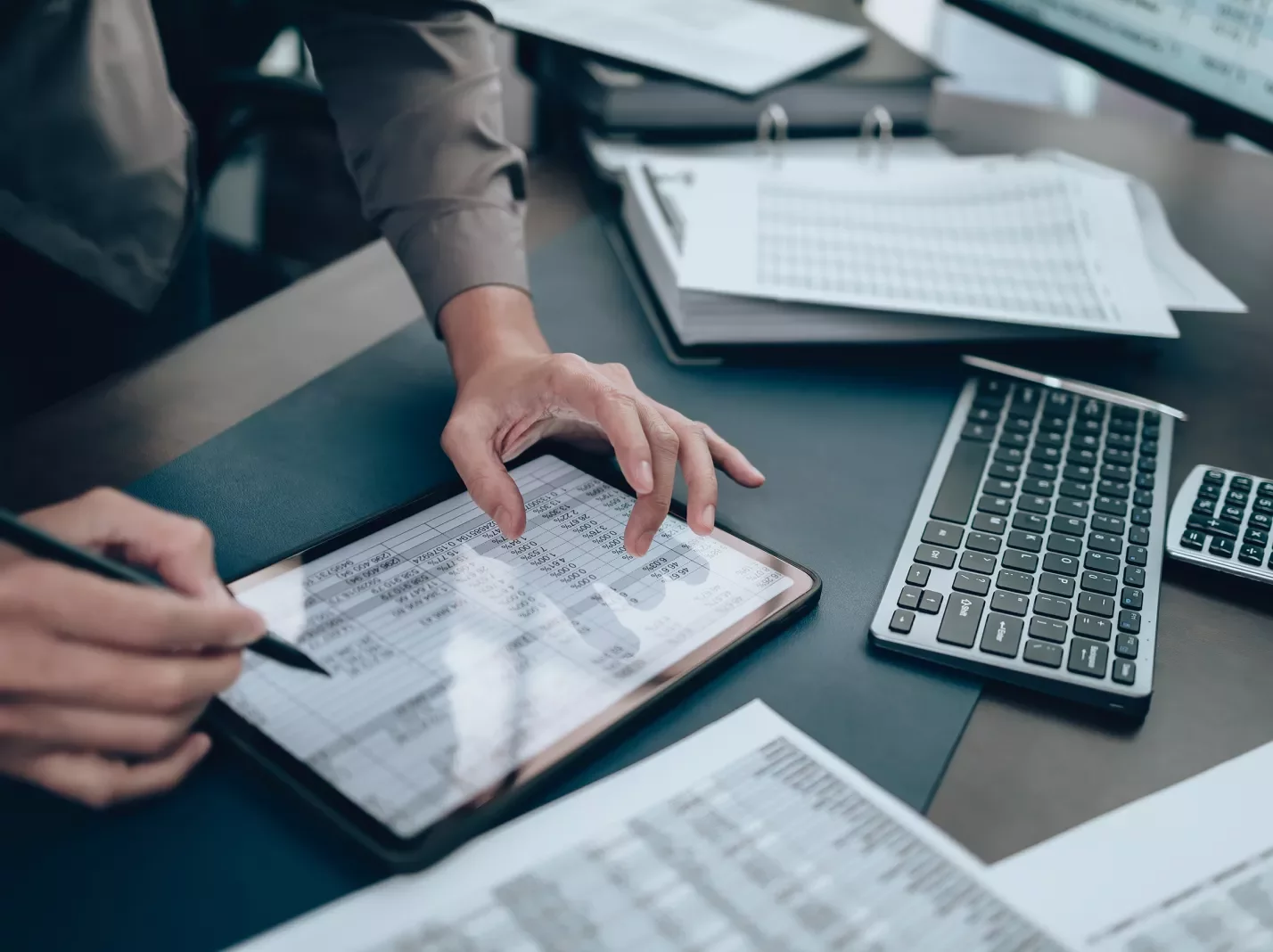 Finance spreadsheet on a tablet screen with computer keyboard and paperwork nearby