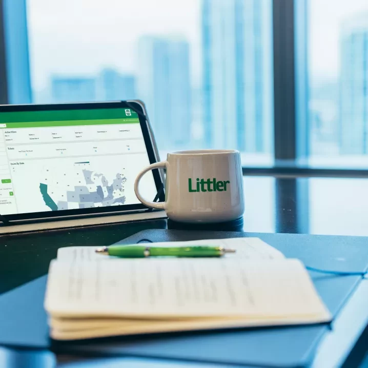 Desk with papers, Littler coffee mug and a tablet screen showing Littler onDemand