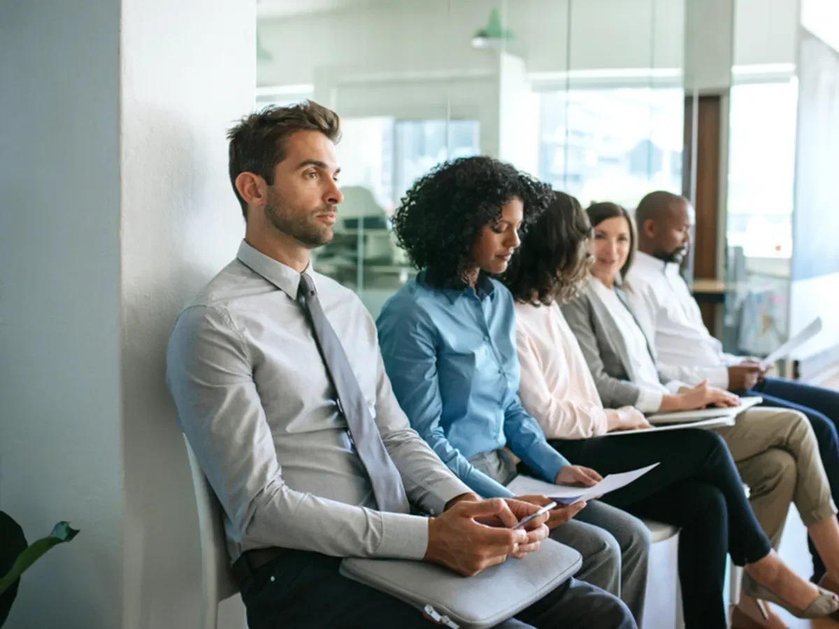 People sit in chairs waiting in a lobby for job interviews