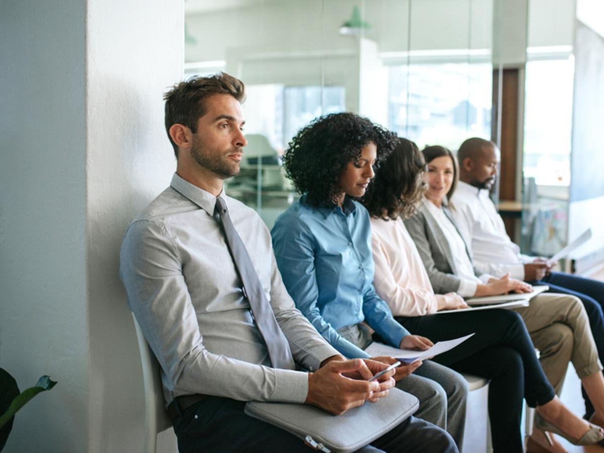 People sit in chairs waiting in a lobby for job interviews