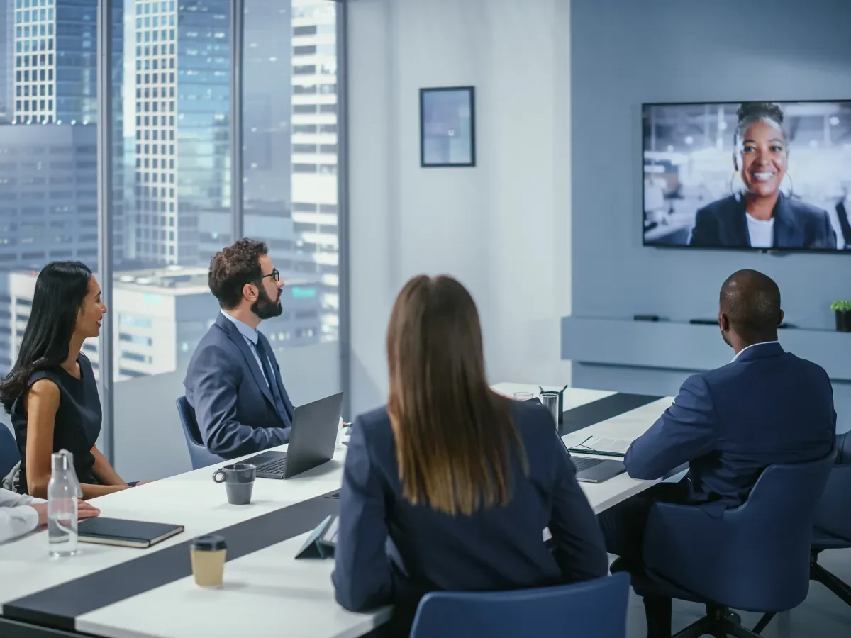 People around a conference room table looking at another participant on screen