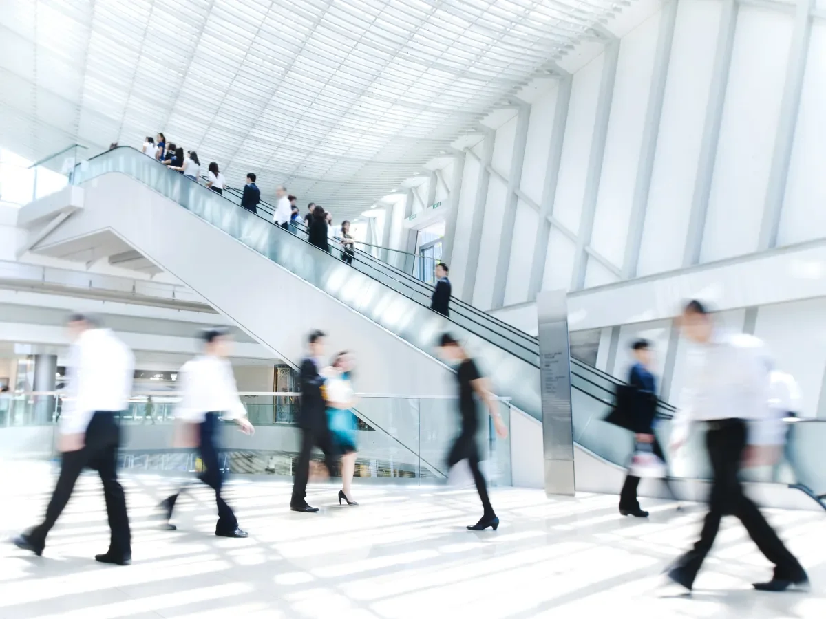 Blurred people walking in an office building lobby with a staircase in the background