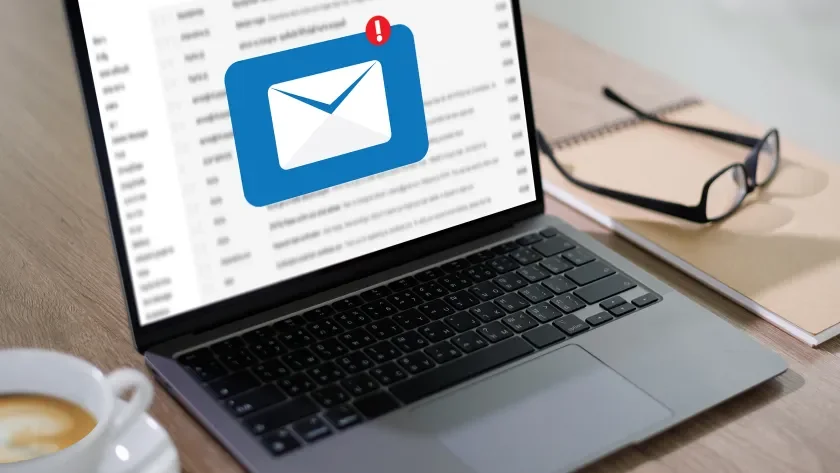 An open laptop with email on the screen and glasses nearby