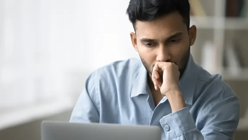 Man with a serious expression and hand to face looking at a laptop screen