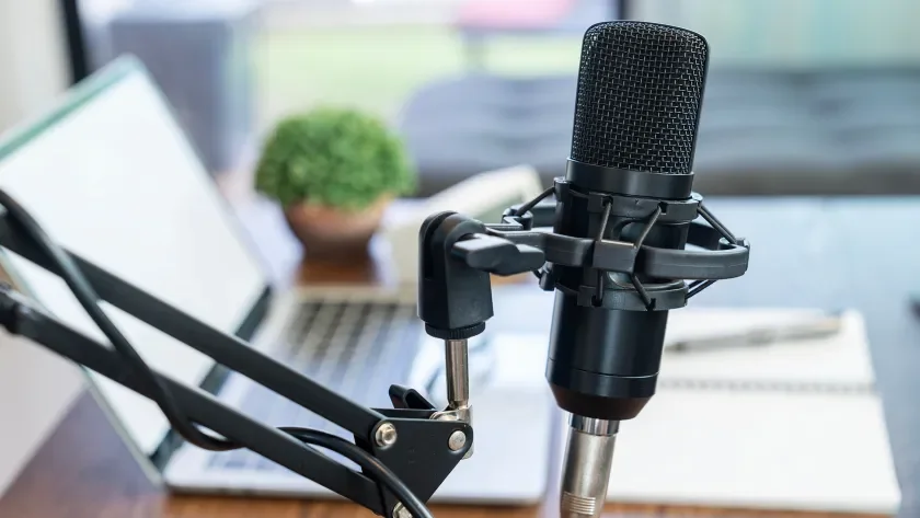 Podcast microphone at a desk in front of a laptop and notebook
