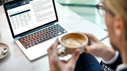Man with coffee reading Littler's Global Guide Quarterly on a laptop