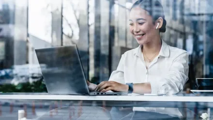 View through a reflective window at a woman looking at a laptop screen