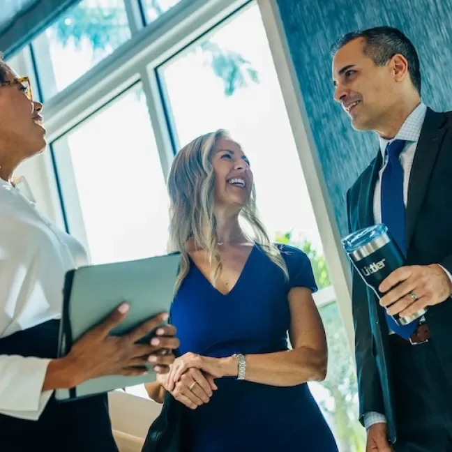 Two women talking to a man in a suit inside an office building