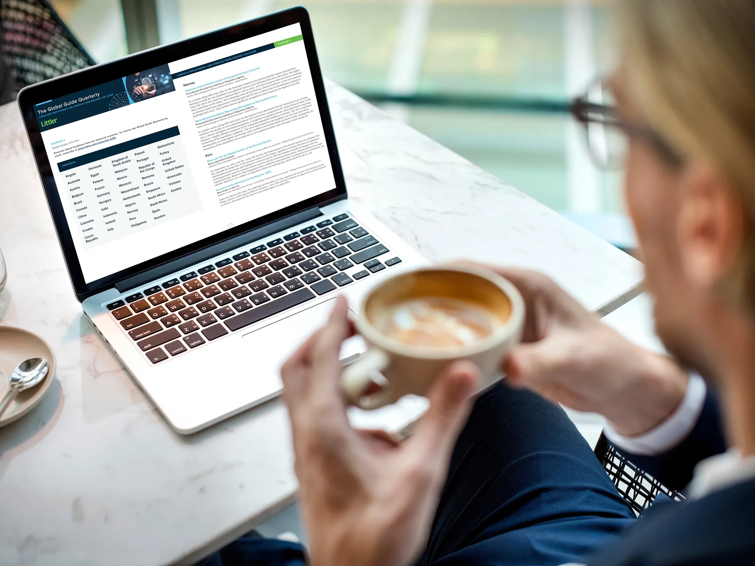 Man with coffee reading Littler's Global Guide Quarterly on a laptop